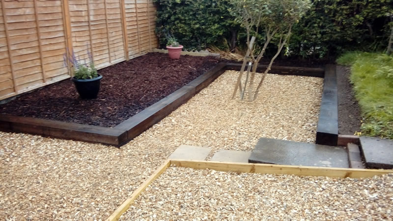 Winch wen garden complete oblong sleeper area next to fence dark chippings on floor light brown chippings between other sleepers trimmed tree in centre